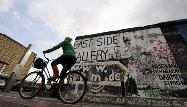 A woman cycles past a portion of the Berlin Wall on October 16, 2008 at the East Side Gallery in Berlin. The East Side Gallery, a more than one kilometre long section of the Wall decorated with paintings by international artists, is to be restored, as most of the paintings are badly damaged by erosion, graffiti and vandalism. AFP PHOTO BARBARA SAX (Photo credit should read BARBARA SAX/AFP/Getty Images)