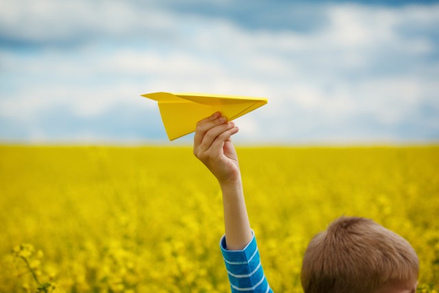 Paper airplane in children hands on yellow background and blue sky in coudy day